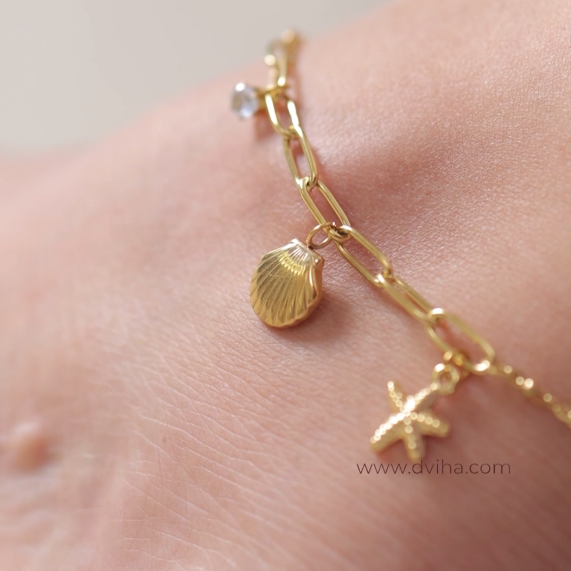 Gold anklet with charms on a person's ankle against a neutral background